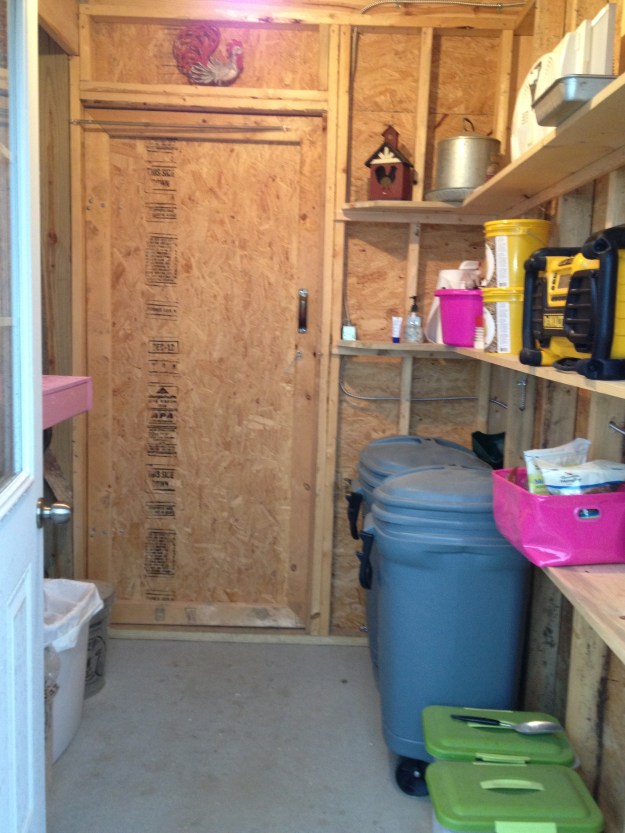 The feed room is the first room you walk into when entering the coop. I store the layer and scratch grain in the large blue containers. The small green containers hold the grit and oyster shell. The chicken treats of mealworms are in the little pink bag. In the far pink bucket are my cleaning supplies.